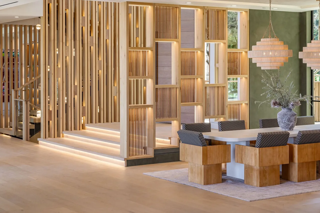Dining area features a white table with wooden block chairs and unique vertical wood panel partitions with integrated lighting.