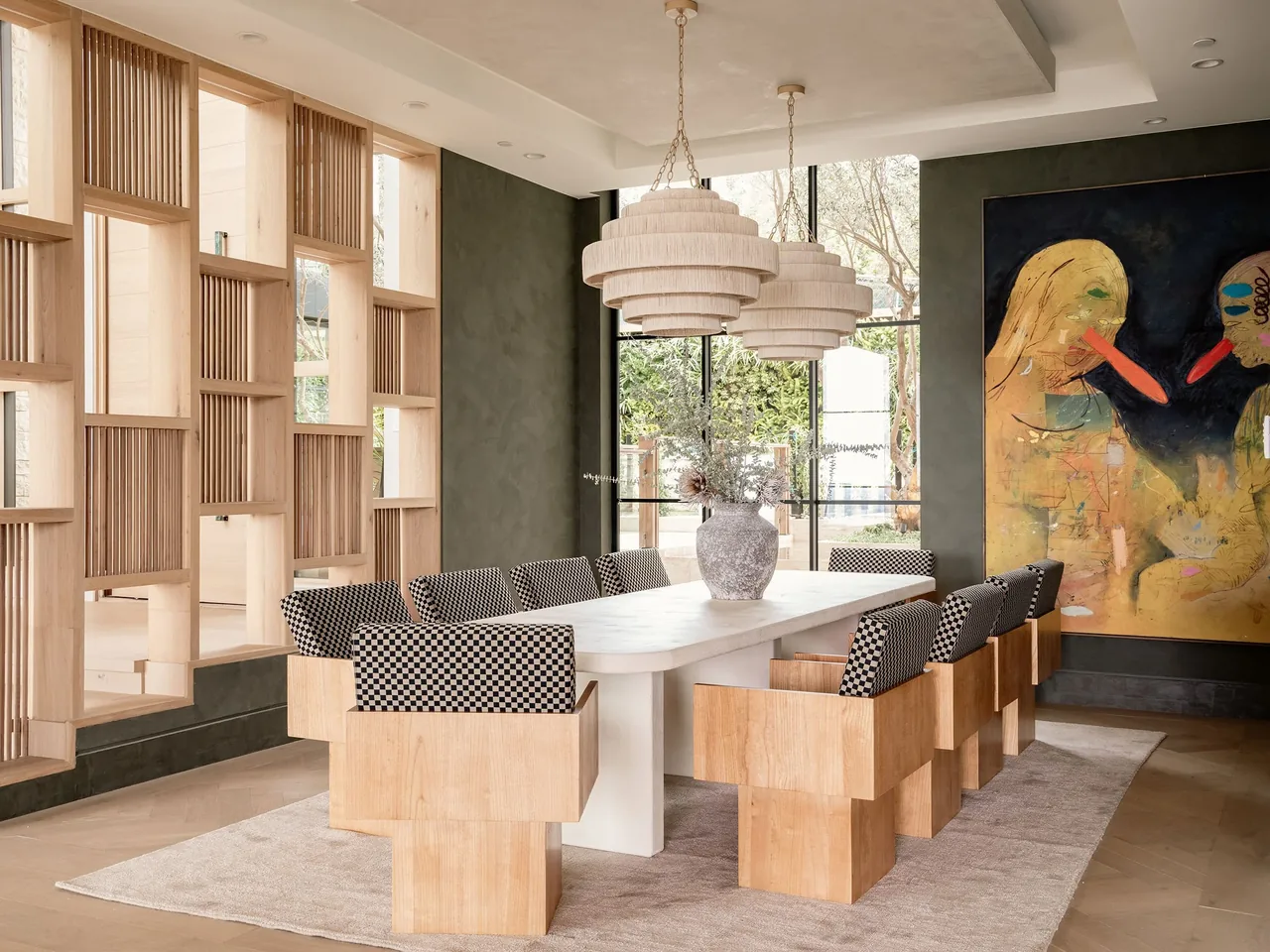 Dining area with a wooden slat wall, artistic painting, and large windows providing garden views.