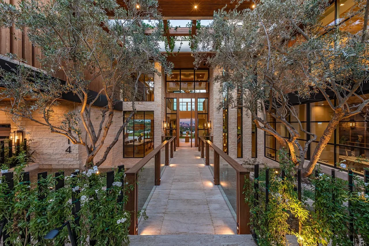 Courtyard walkway with glass railing and integrated lighting at the entrance of a modern hillside mansion.