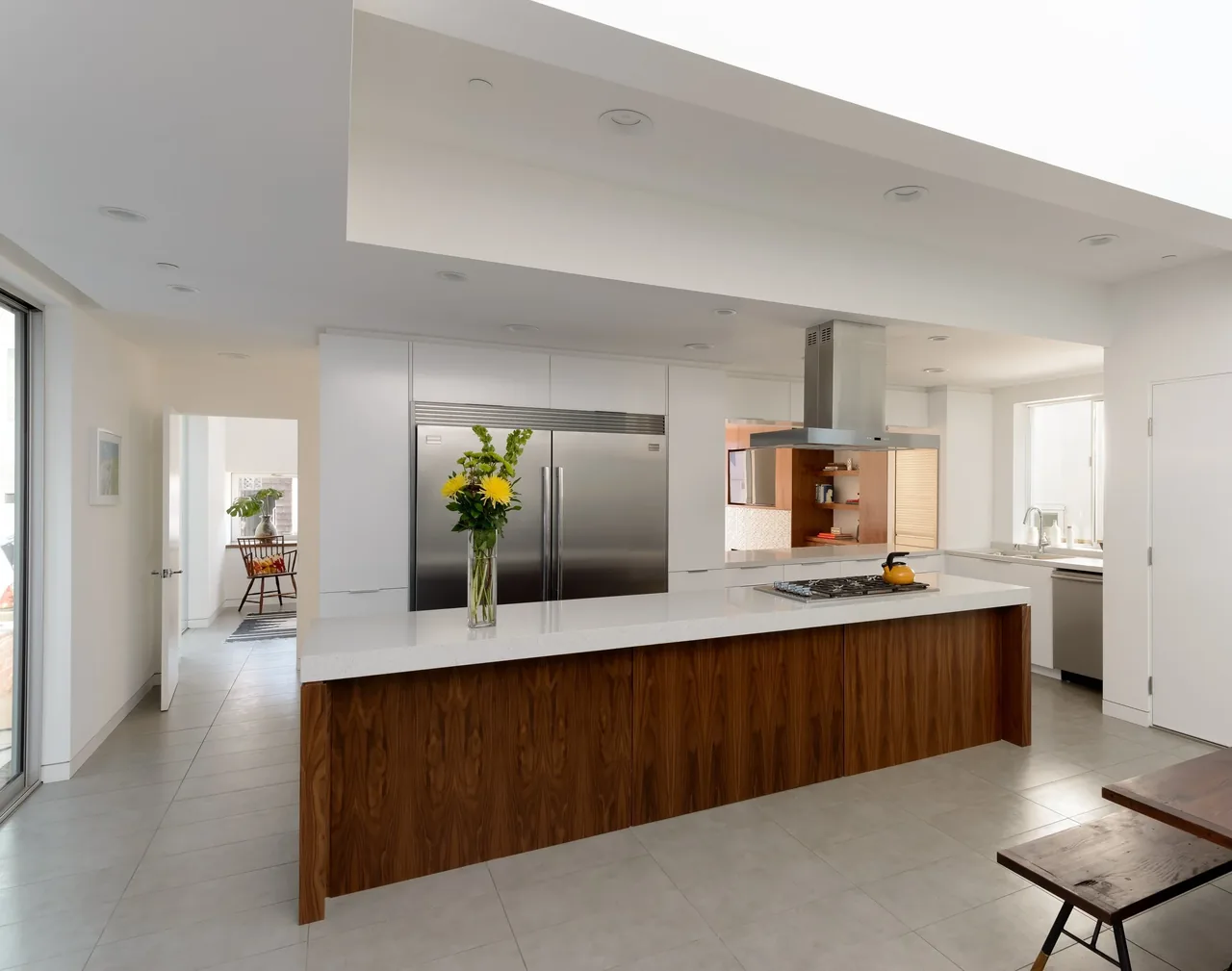 The kitchen features a wood-paneled island, large stainless steel refrigerator, and a stainless steel range hood.