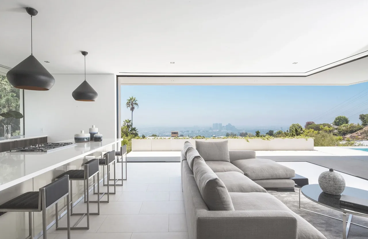 Open living area with kitchen island and large sectional sofa opens to a wide view of landscape and city.