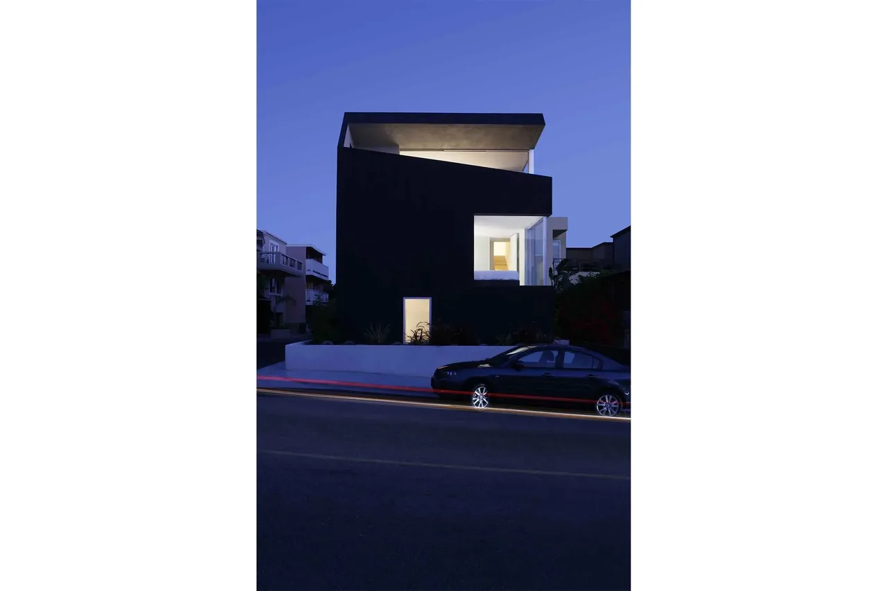 The three-story Surfhouse features a bold angular flat roof and large window openings, shown here at dusk with interior lights on.