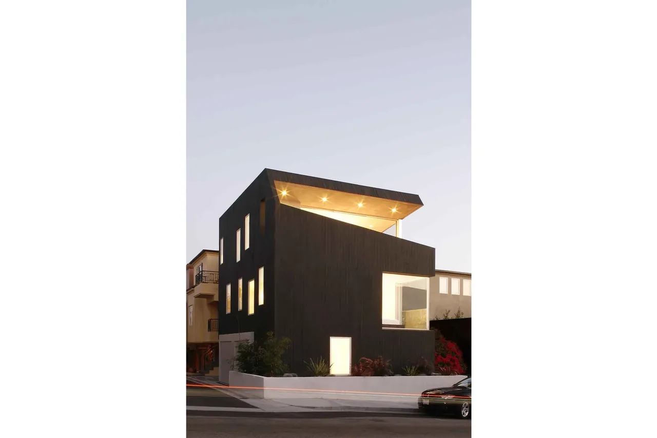 The Surfhouse is a three-story modern residence featuring dark wood siding and large windows under an angled flat roof.