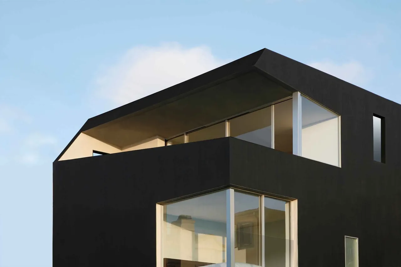 Surfhouse features black exterior walls with expansive corner windows and a distinctive angular roof overhang.