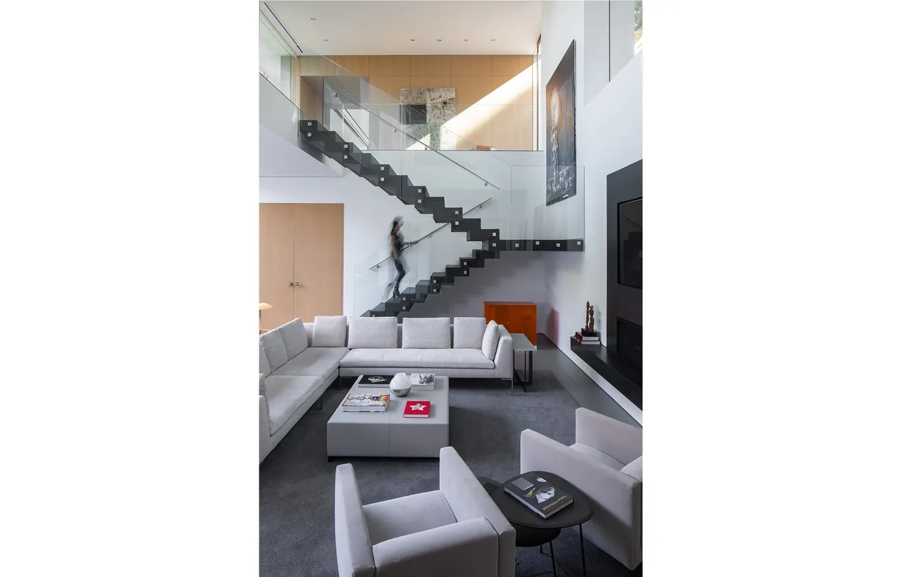 Living room features a floating staircase with glass railing and modern gray seating in a double-height space.