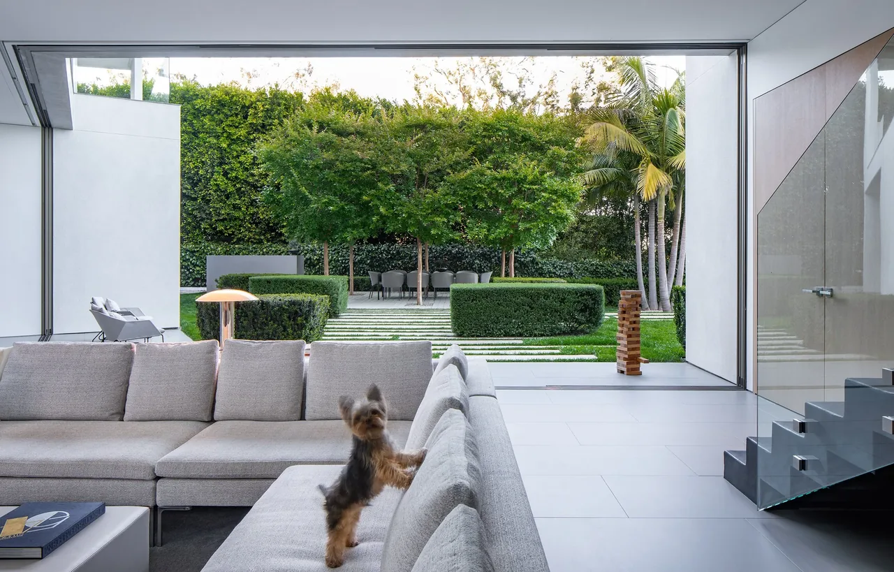 Living room opens to a manicured garden with trimmed hedges and mature trees in the backyard of the aMahouse project.