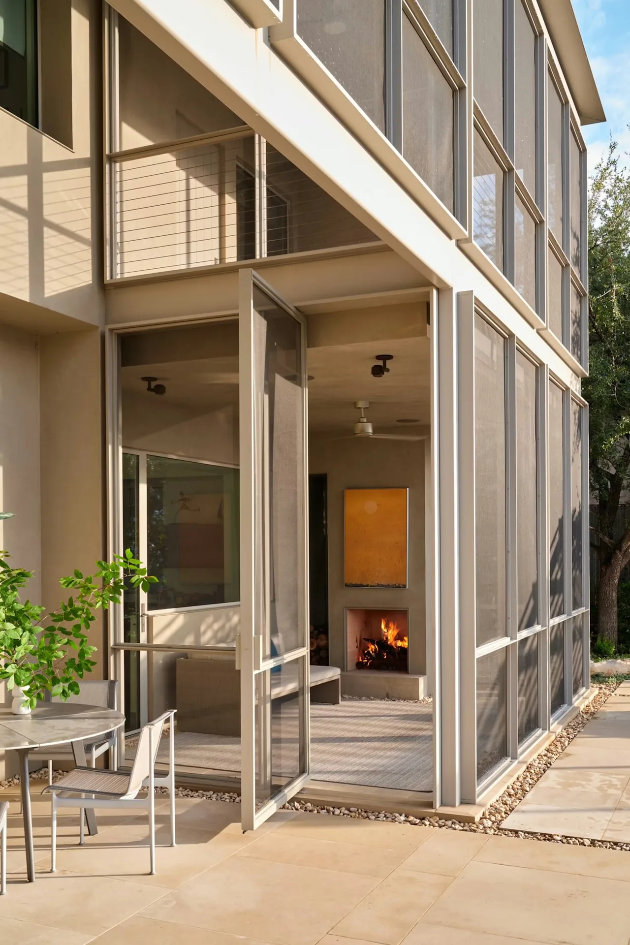 Open glass door connects outdoor patio with an indoor living space featuring a fireplace in Residence on Mount Barker by Andersson Wise Architects.