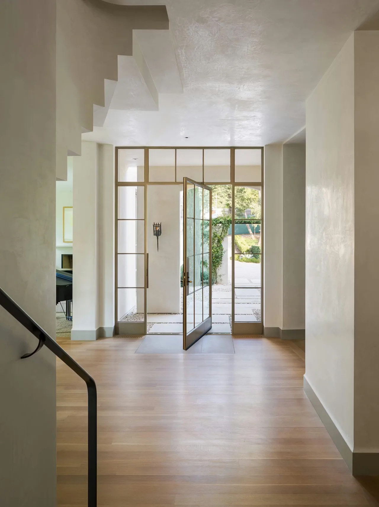 The entryway of the Tarryhill Residence features a metal-frame pivot door and a rustic wall-mounted lantern by Andersson Wise Architects.