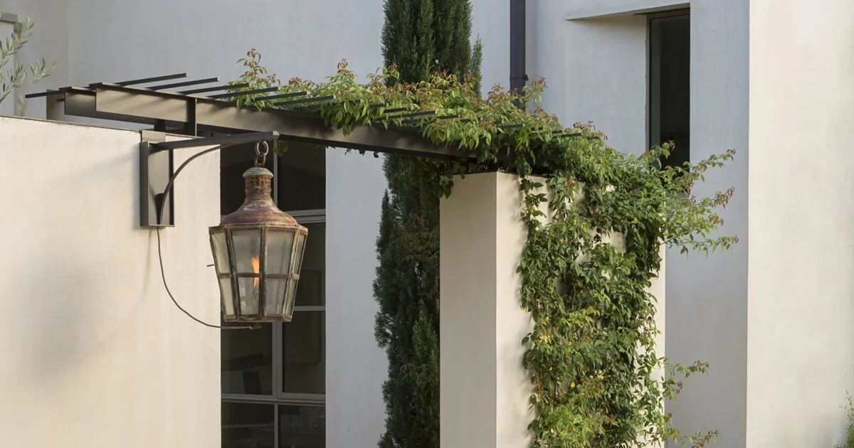 An outdoor lantern hangs from a metal trellis covered in greenery at the Tarryhill Residence exterior.