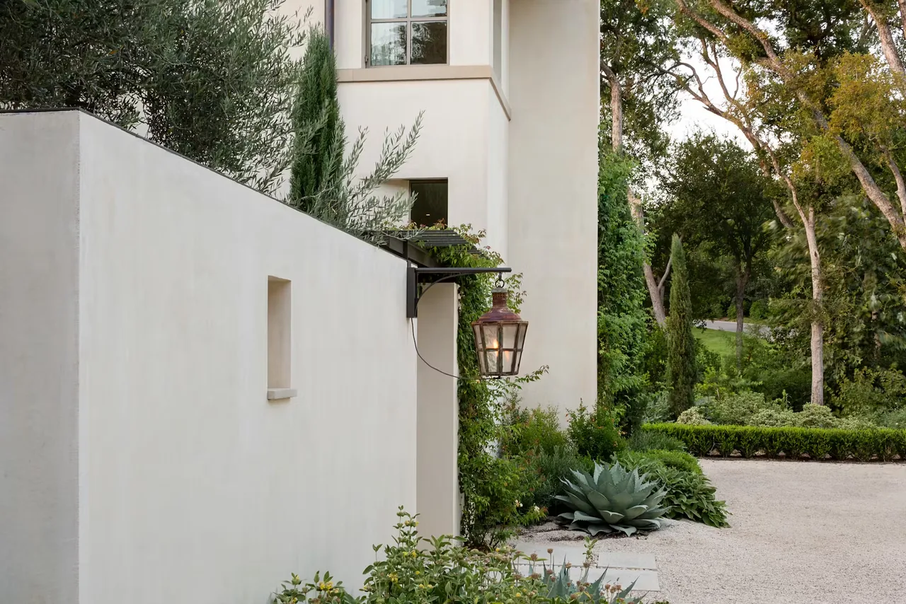 Exterior view of the Tarryhill Residence showing a white stucco wall, metal trellis with climbing vines, and a rustic lantern.