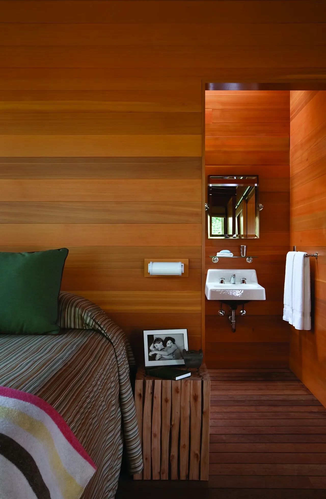 Bedroom corner featuring wood plank walls and flooring, a small sink with a mirror, and a wood bedside table with decoration.