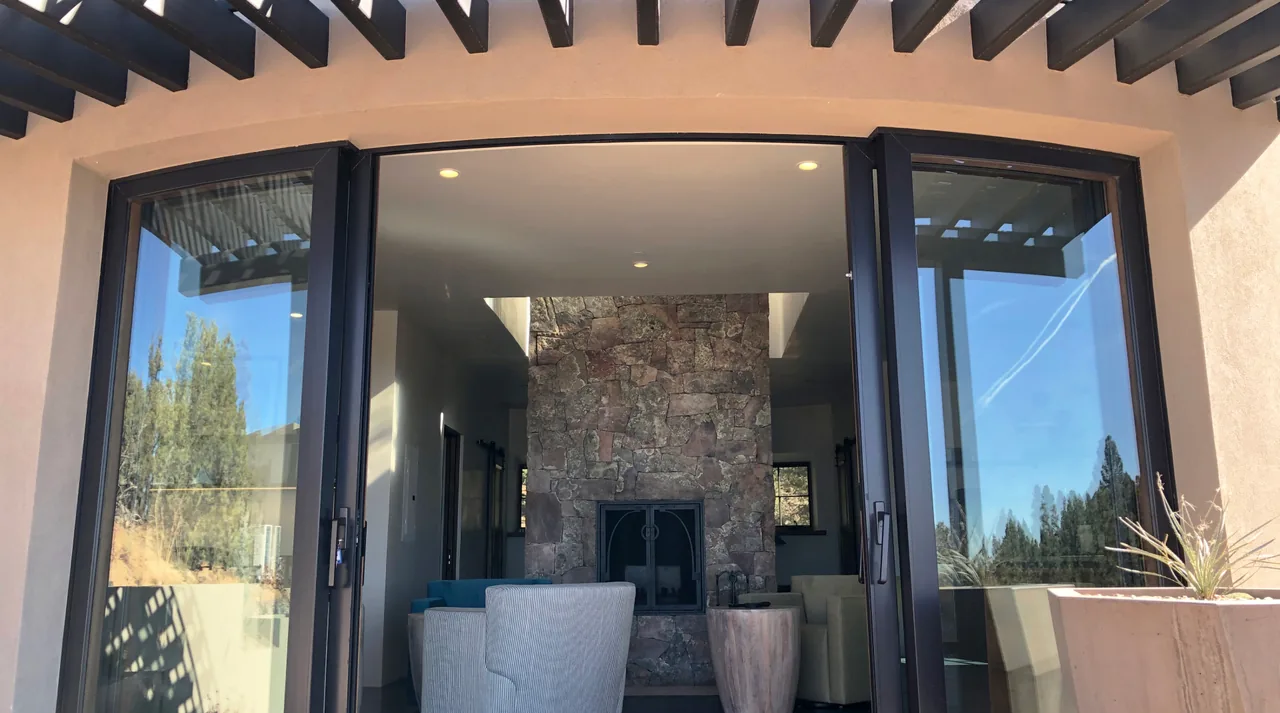 Interior stone fireplace visible through large folding glass doors beneath a wooden pergola.