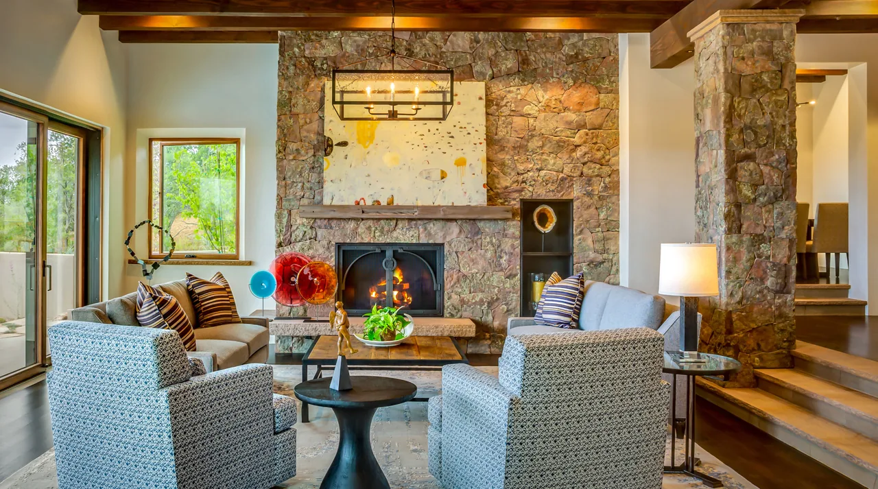 Living room features a stone fireplace with wooden mantle, ceiling beams, and comfortable seating arranged around a central coffee table.