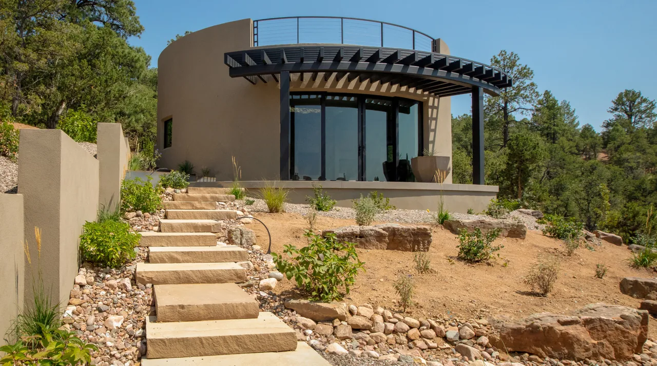The Cummings project features curved stucco walls with an arched metal awning and stone retaining walls in natural landscaping.