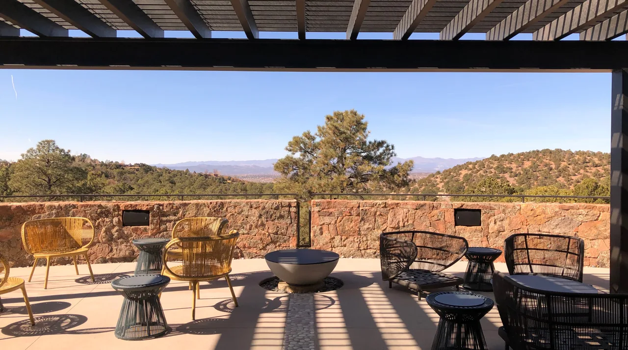 Outdoor living area with a wooden pergola and stone retaining wall framing a scenic view of hills and trees.