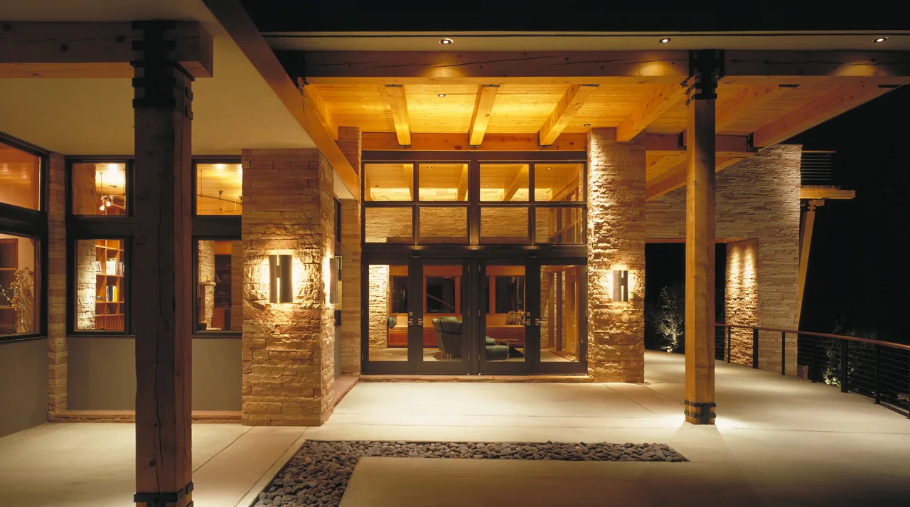 Night view of the front entrance featuring stone columns, exposed wooden beams, and large glass doors.