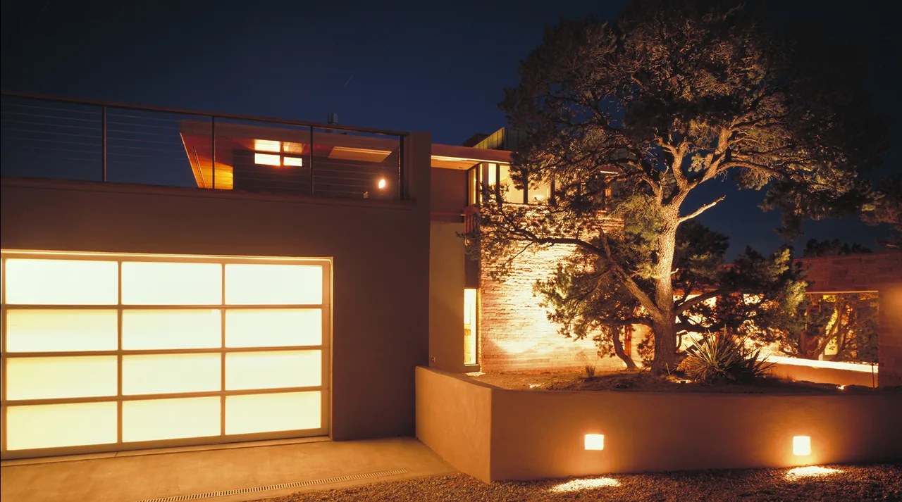Greene project features a multi-level modern house with illuminated garage doors and landscaped rocky hillside at night.