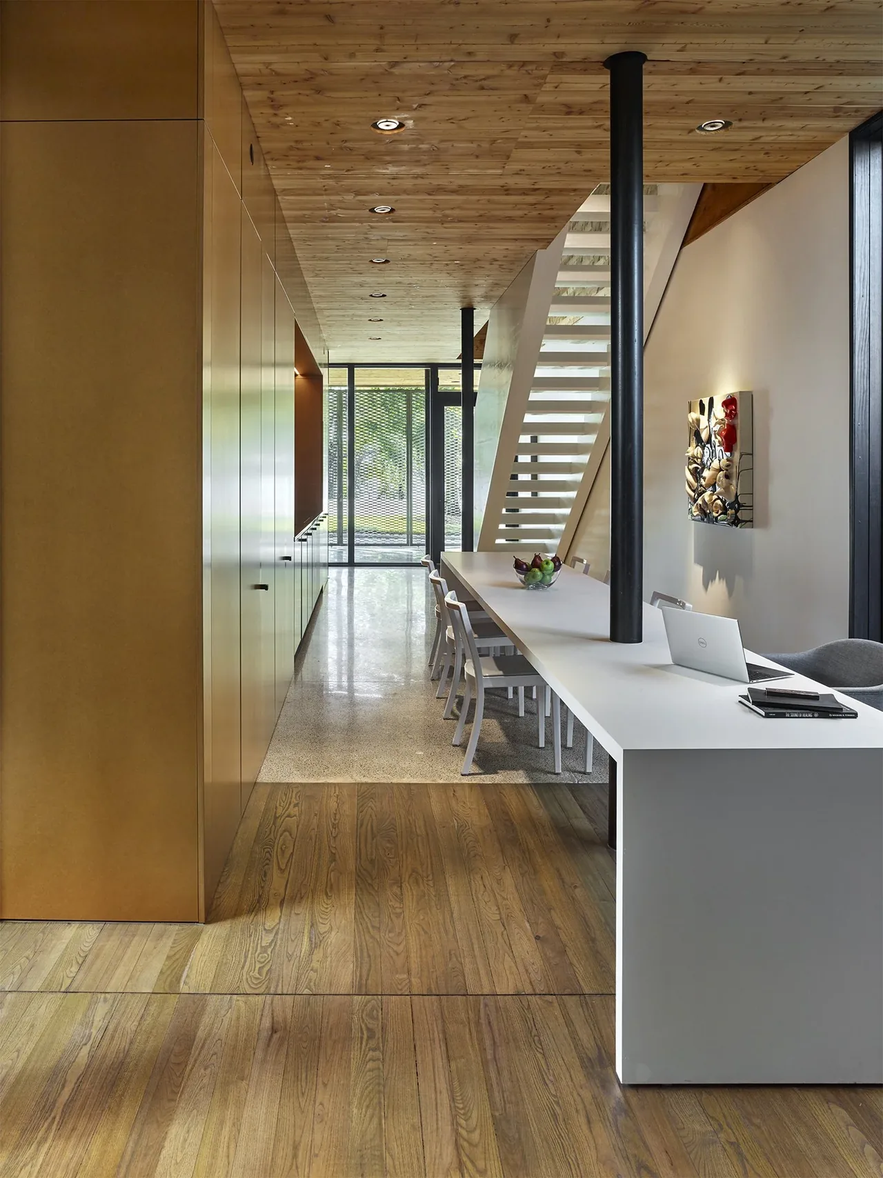 Dining area with a long white table, white chairs, a wooden ceiling, and a minimalist white staircase.