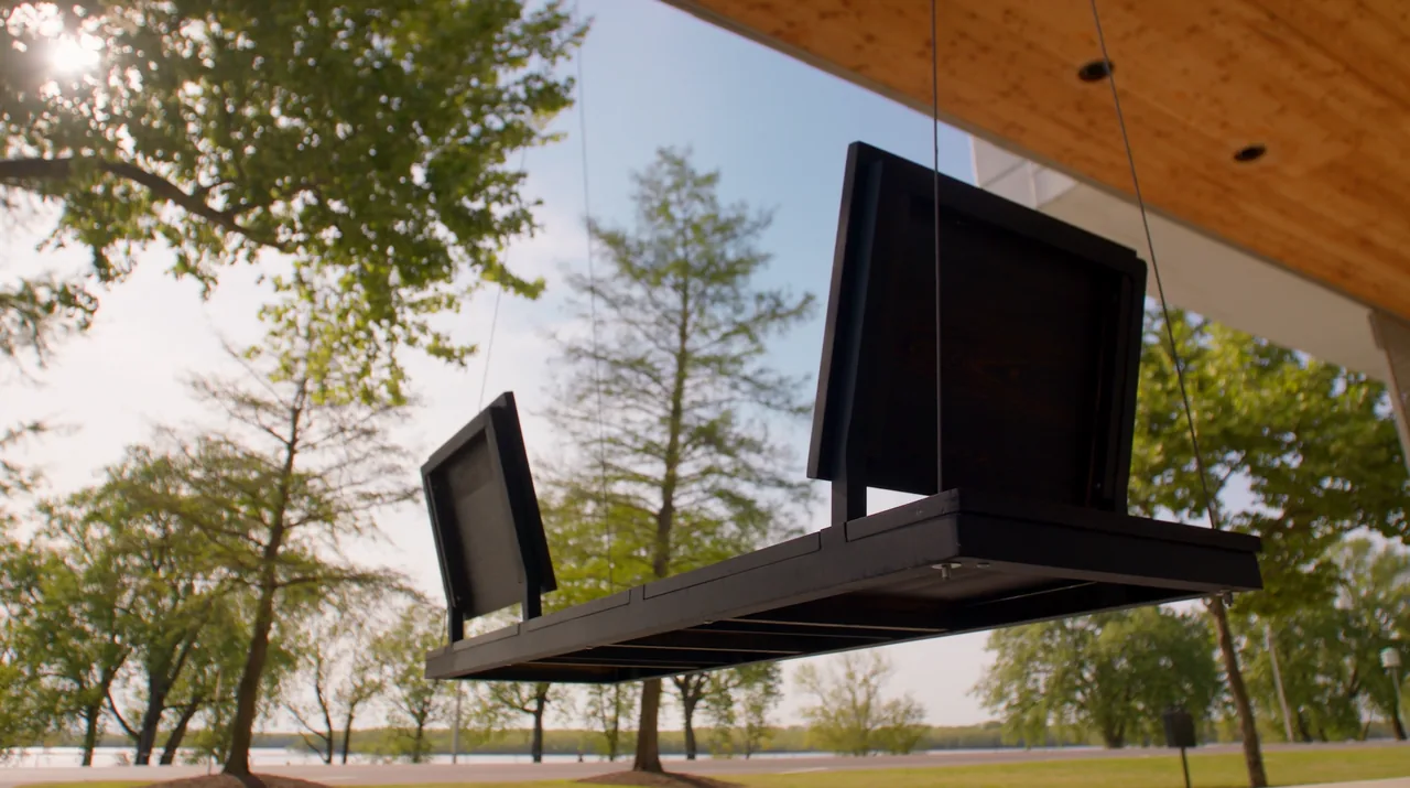 Suspended dark wood bench on a covered patio overlooking trees and a body of water.