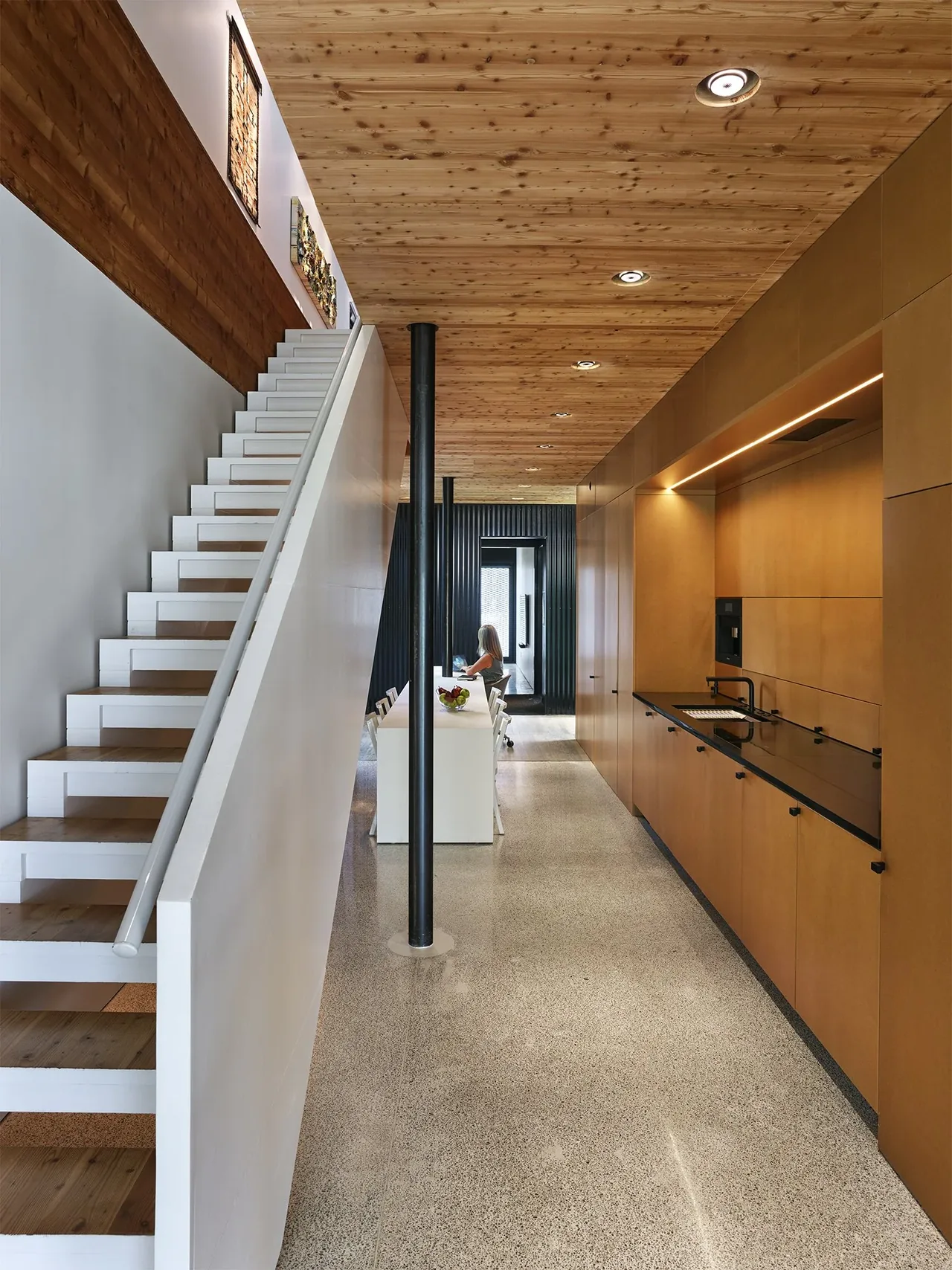 A modern kitchen and dining area with a wooden ceiling, white floating staircase, and terrazzo flooring.