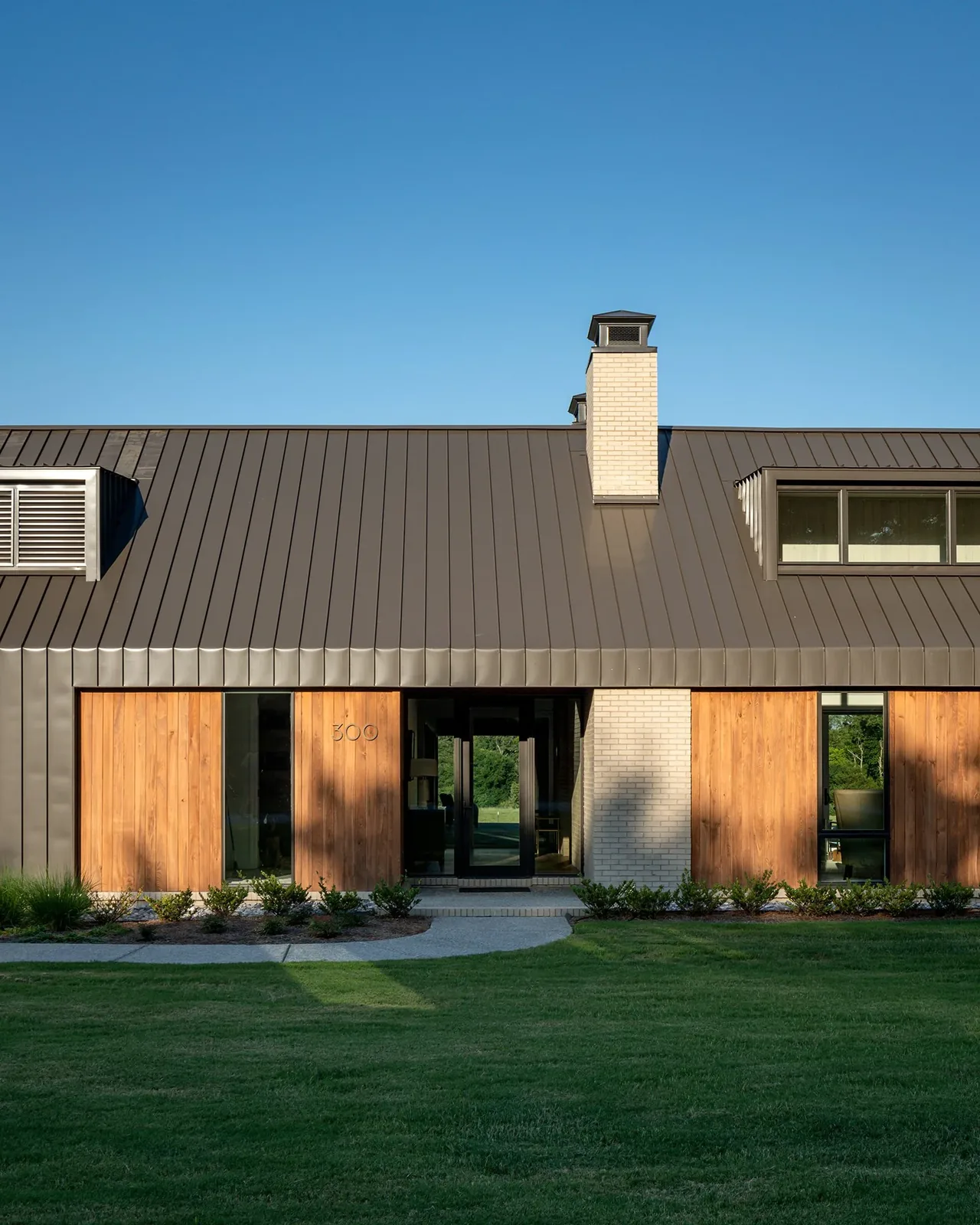 Fleetview Residence with steep metal roof, vertical wood siding and a central light brick chimney.