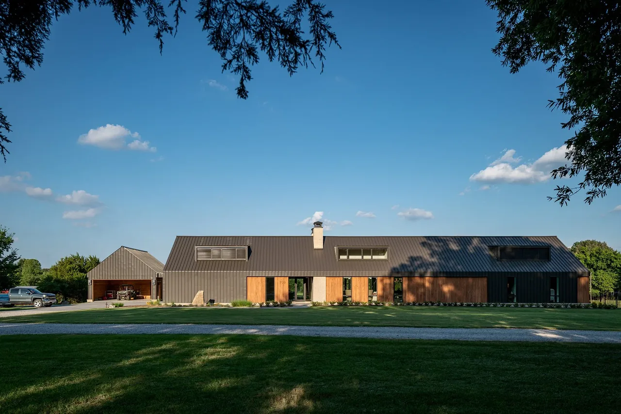 Fleetview Residence features a modern long pitched roof home with dark metal siding and wood accents by Archimania.