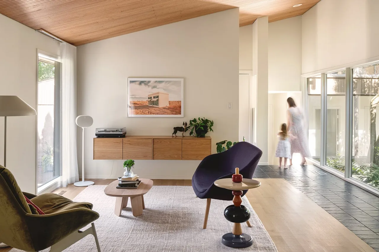 Living room featuring a wood-paneled ceiling, floor-to-ceiling windows, and a mix of modern seating and a low coffee table.