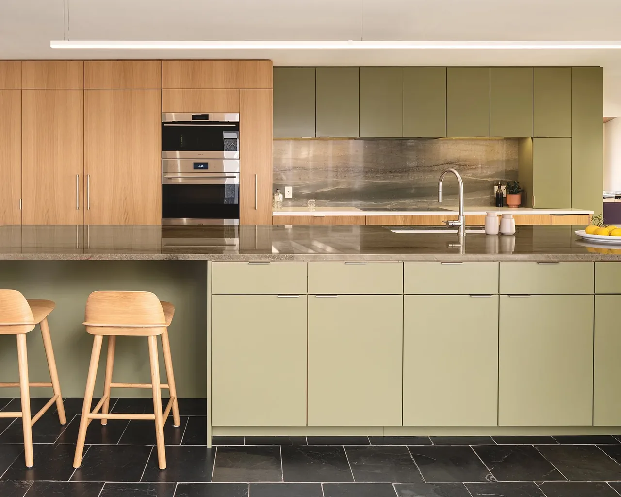 The kitchen features olive green and wood cabinetry, a gray stone countertop island with a sink, and built-in stainless steel appliances.