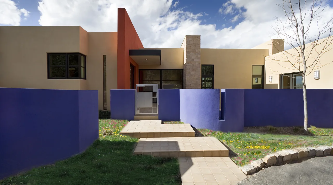 The Lehman project by Archaeo Architects features a modern home with a beige and orange facade and a distinctive blue fence enclosing the front yard.