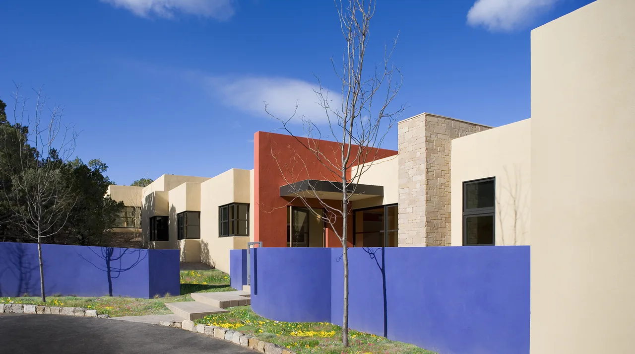 Lehman project exterior featuring beige stucco, a vibrant orange accent wall, and a curved blue stucco fence under a clear blue sky.
