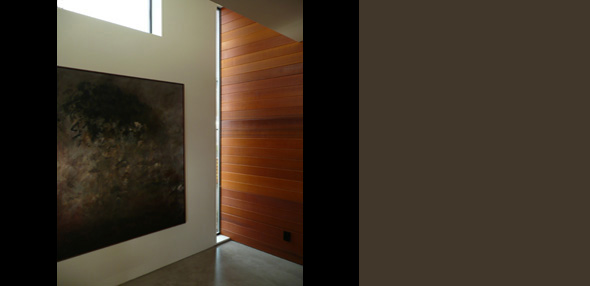 Interior shot shows a tall narrow window next to wood paneling and a large abstract painting on a white wall.