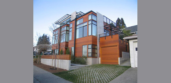 Three-story modern residence with wood siding, black window frames, and flat roof with concrete elements.