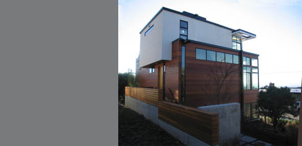 Three-story modern house featuring wood siding, concrete foundation, and large windows, including tall narrow ones near the top.
