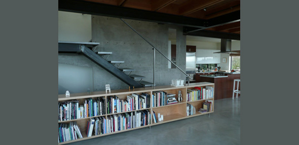 Modern interior showcasing a metal staircase next to a concrete wall and a built-in wooden bookshelf under wooden ceiling beams.