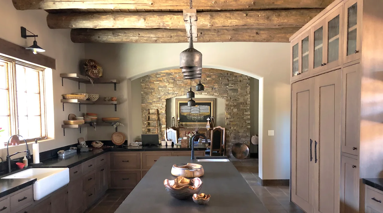 Southwestern kitchen with a stone archway, wooden ceiling beams, and terracotta tile floor at Applegate Residence.