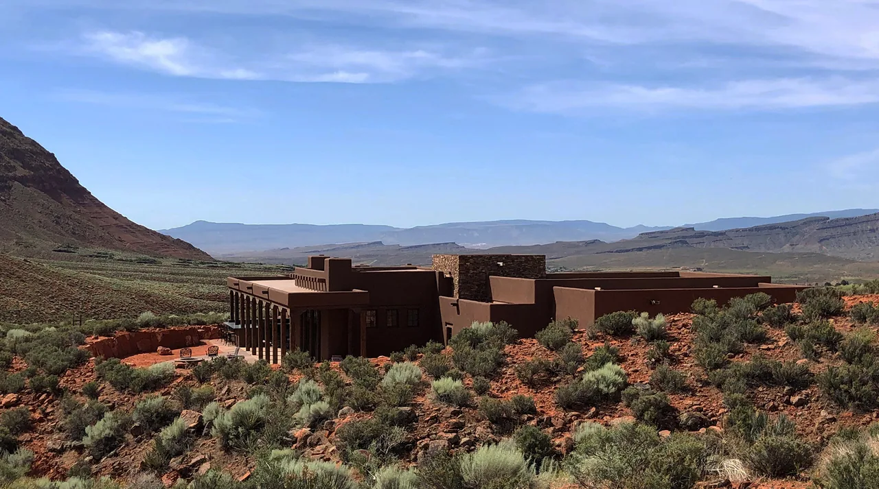 Applegate Residence features adobe-style architecture blending into desert terrain with red sandstone cliffs in the background.