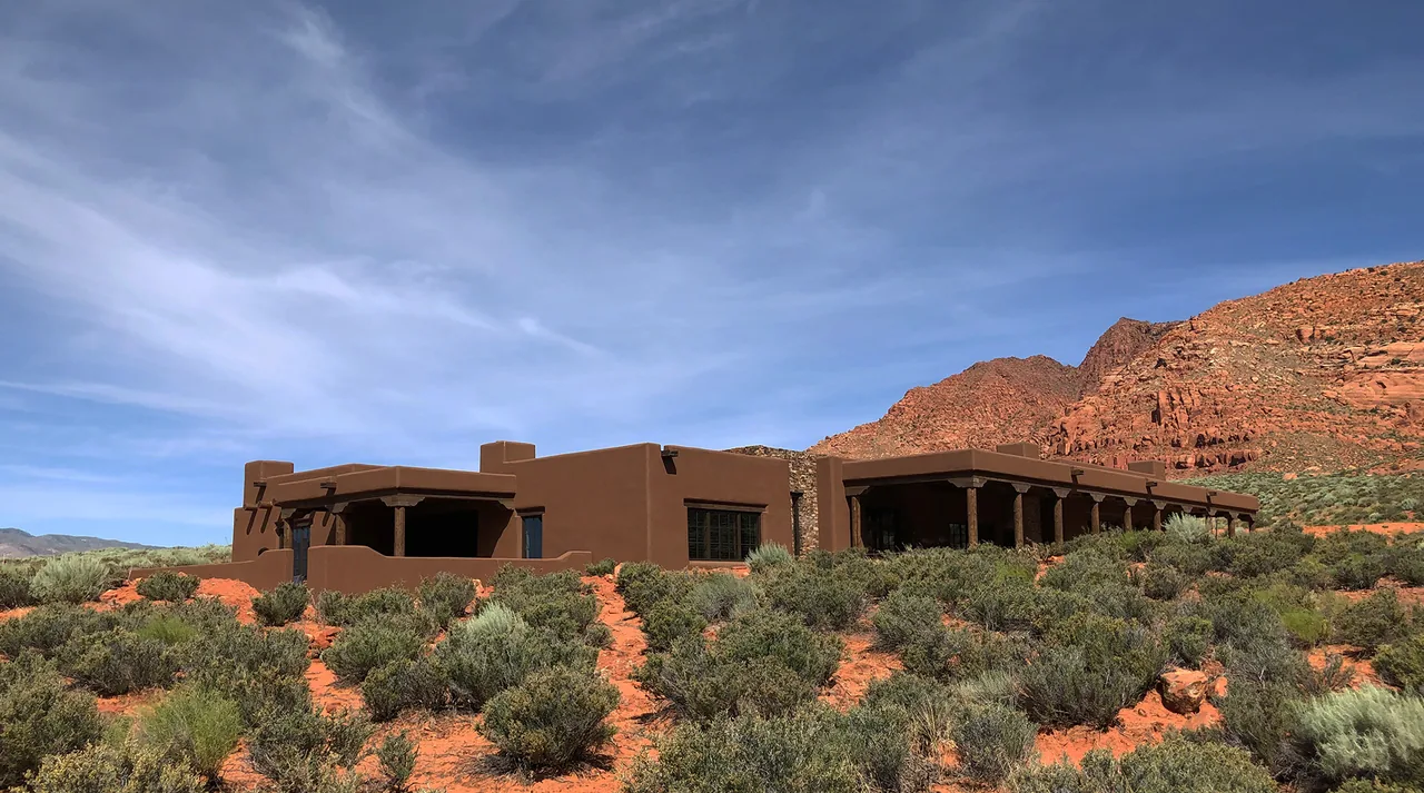 The Applegate Residence features adobe-style architecture with a flat roof, blending into a desert landscape with red sandstone cliffs.