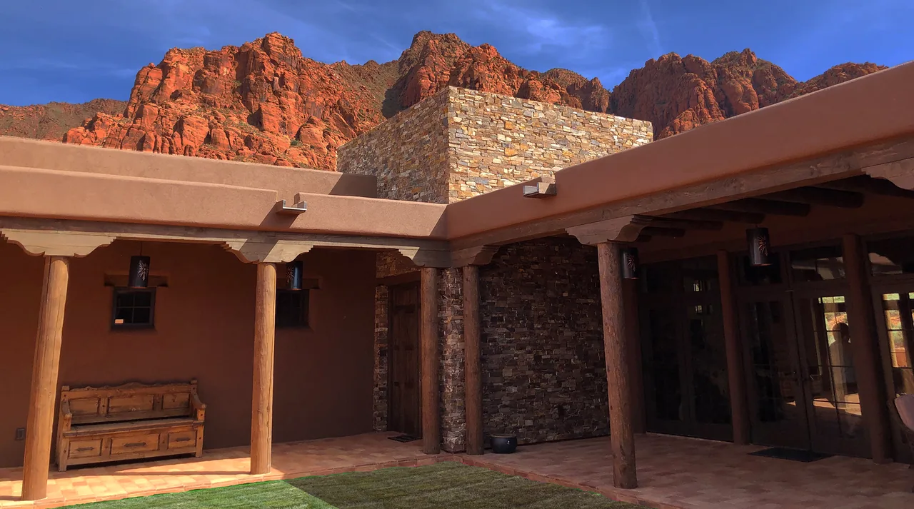 Patio courtyard featuring adobe style walls, wooden bench, terracotta tile flooring, and a stacked stone chimney with a view of red sandstone cliffs.