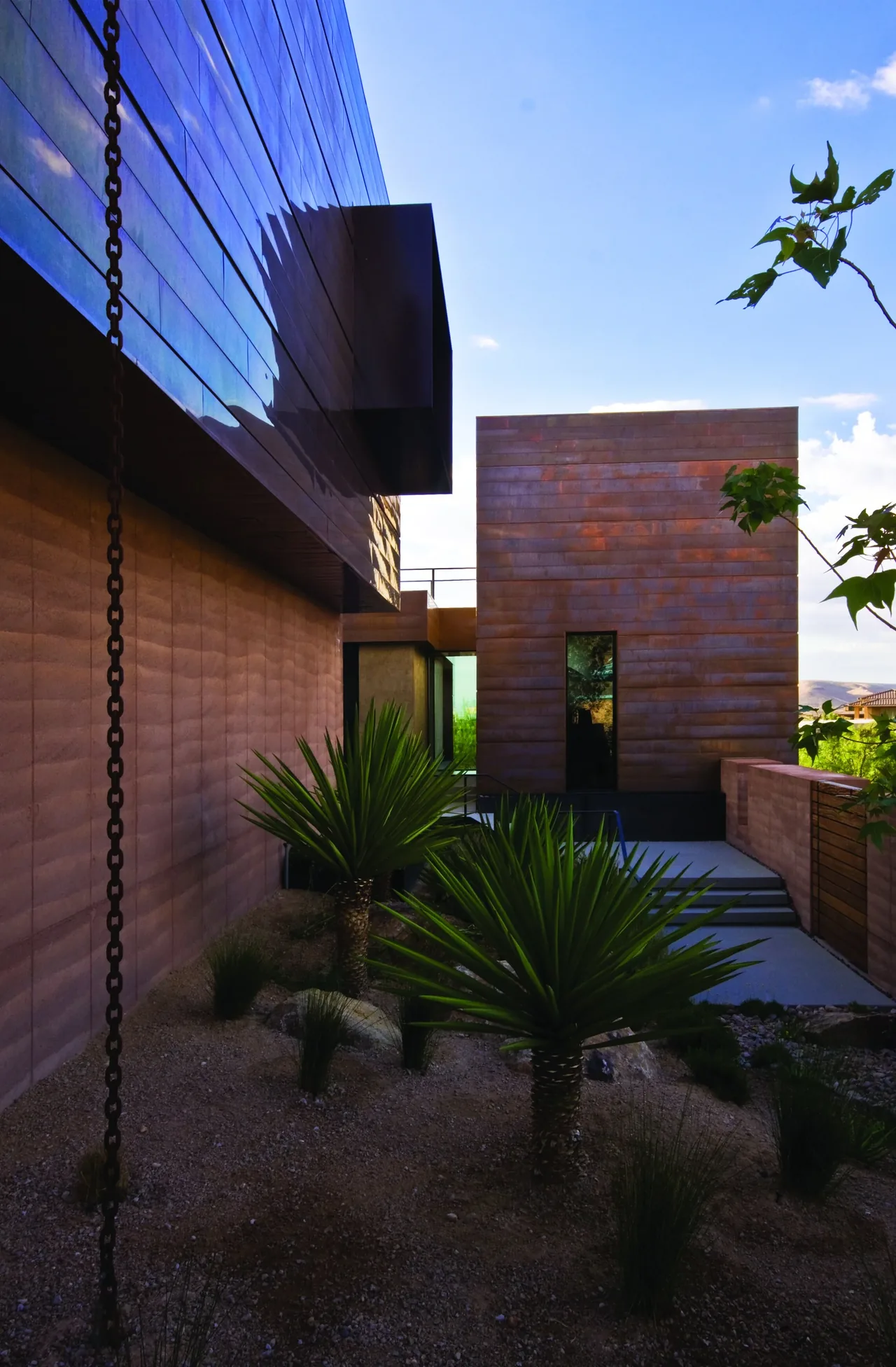 Modern home exterior featuring rust-colored siding and a minimalist patio with desert landscaping.