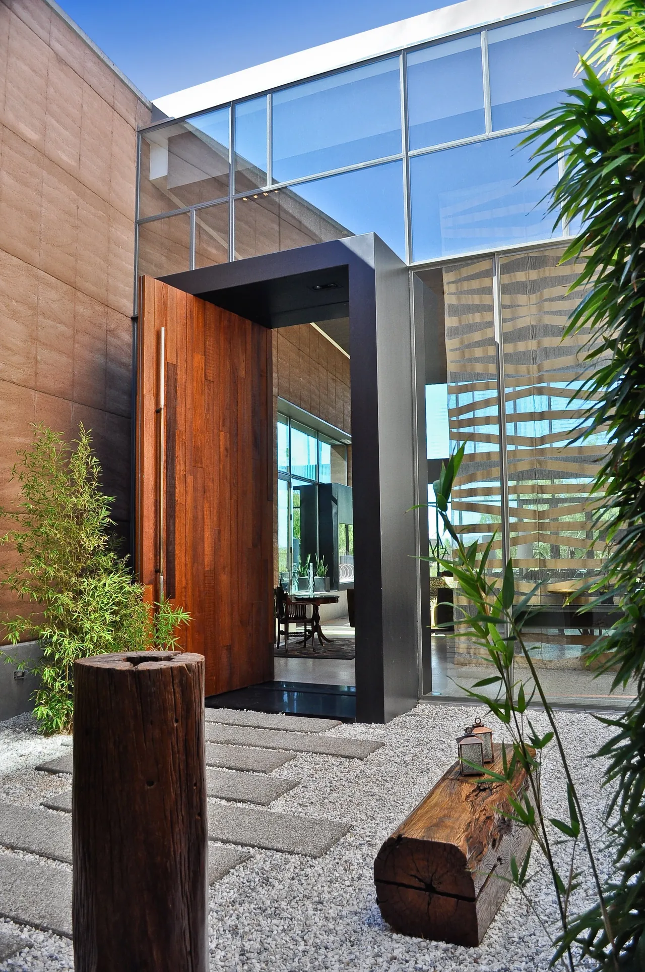 J2 Residence features a massive wooden pivot door entrance under black metal framing with rammed earth and glass walls.