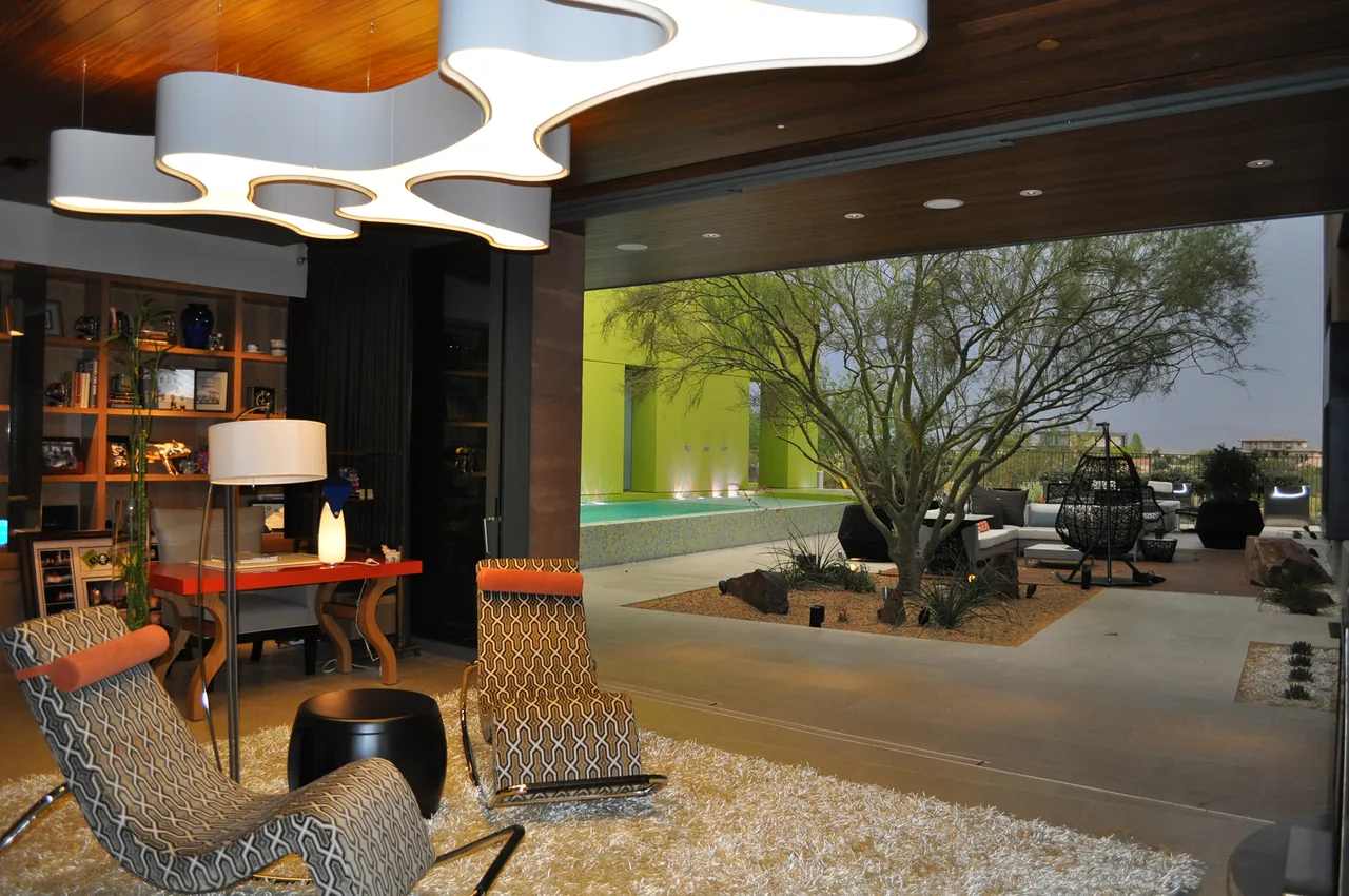Living room opens to an outdoor living area with pool and desert tree at J2 Residence.