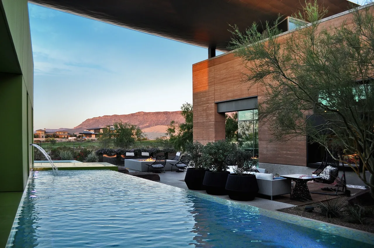 The J2 Residence features a rectangular pool beside rammed earth exterior walls with mountain views at sunset.