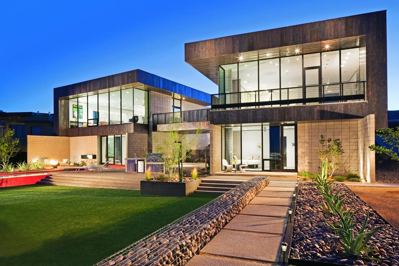 Night view of a modern two-part house with large floor-to-ceiling windows and an illuminated outdoor area with steps and greenery.