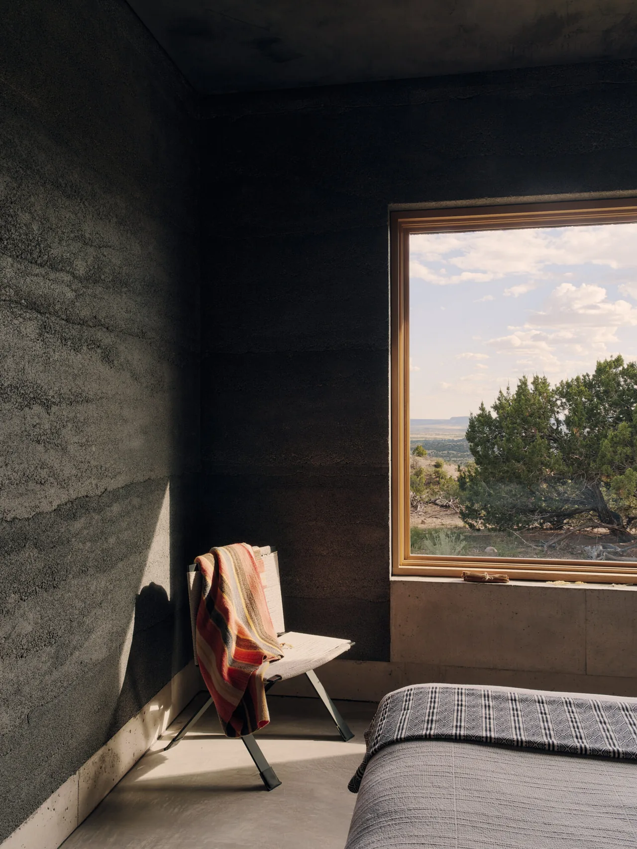 Bedroom corner with textured wall, built-in concrete seating under a large window showcasing a desert landscape view.