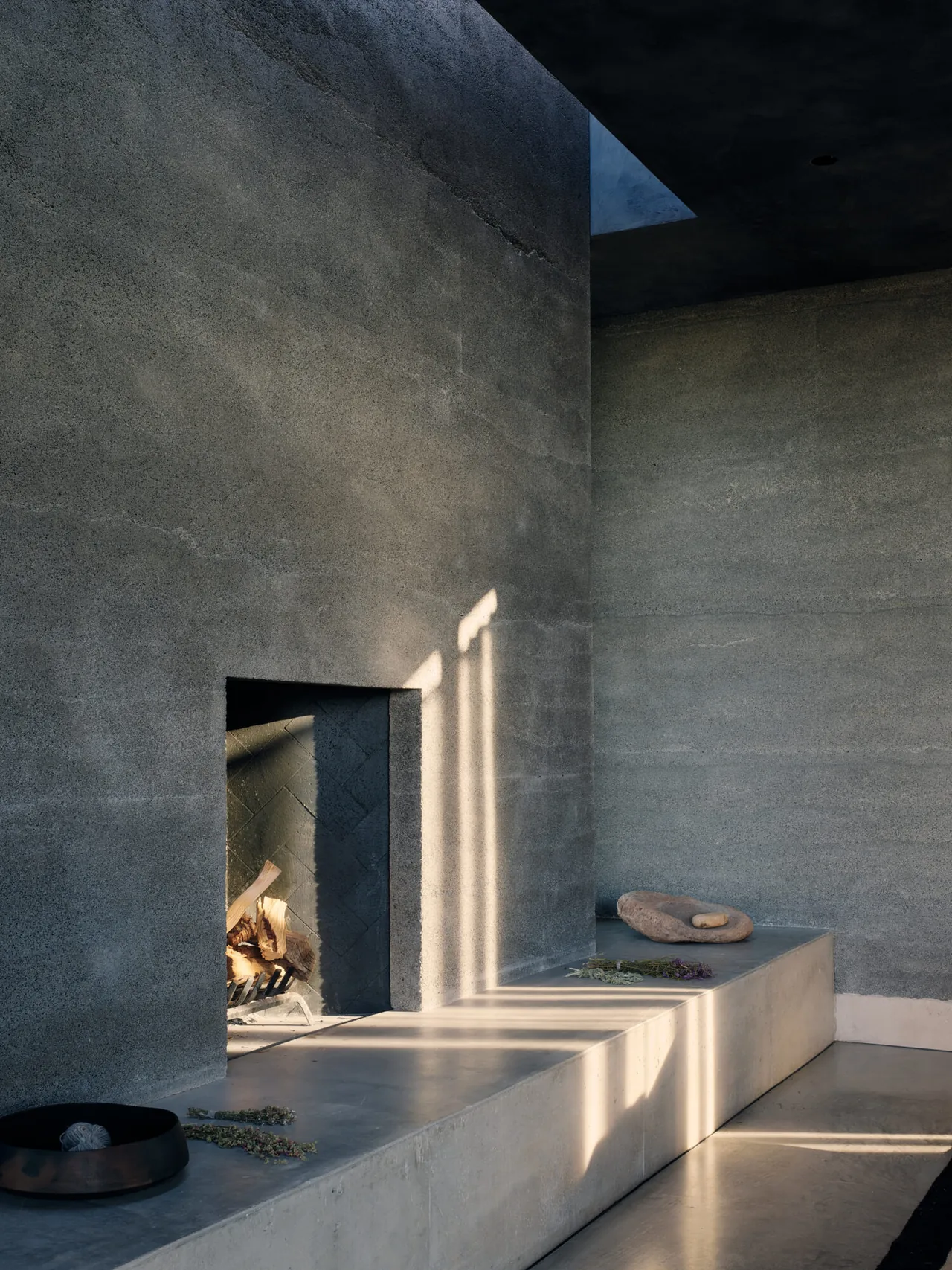 Minimalist concrete fireplace with built-in concrete seat and textured wall surface illuminated by natural light.