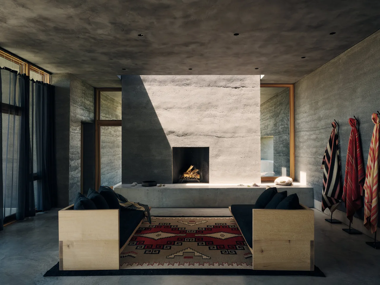 Living room interior features a rammed earth fireplace and paired wood sofas centered on a southwestern-patterned rug.