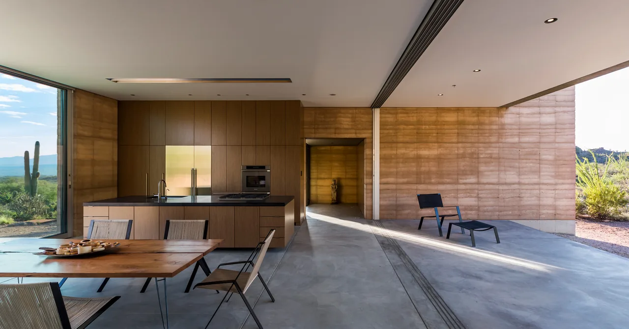 Open kitchen and dining space extends outdoors with rammed earth walls and desert views at Tucson Mountain Retreat.