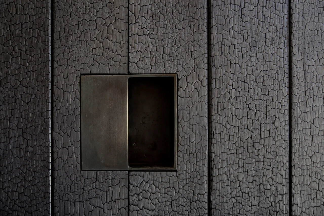 Recessed metal pull handle on a dark wood door with cracked texture at Tucson Mountain Retreat.