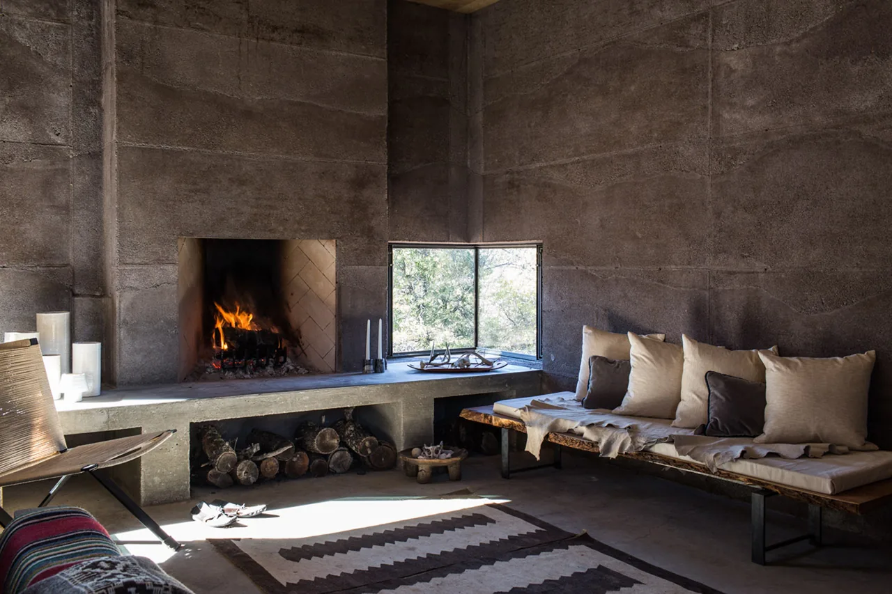 Living area with a fireplace, concrete walls, and a corner picture window framing nature views.