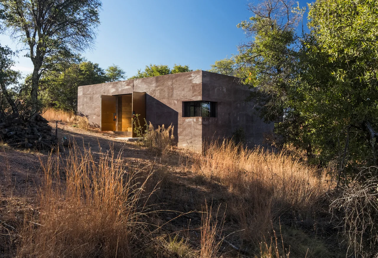Casa Caldera is a concrete block house nestled in a natural setting, featuring a recessed entry and small horizontal windows.